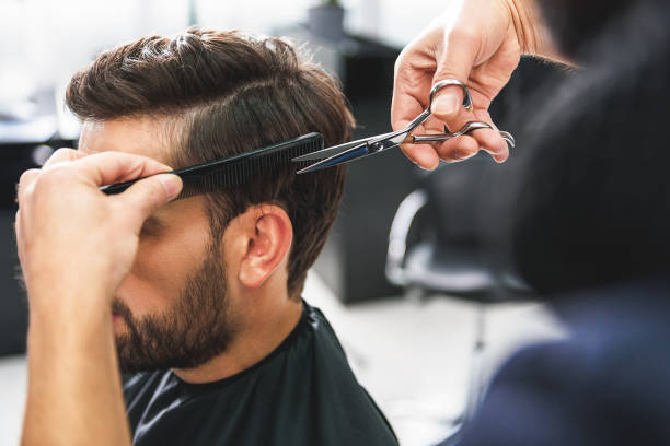close up of hairdresser arms cutting and combing male hair